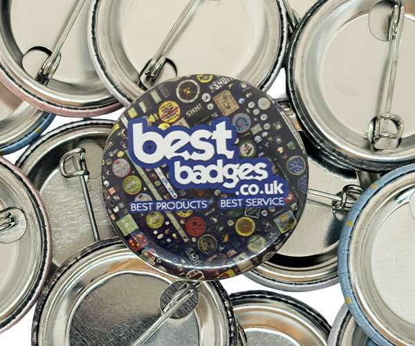 A pile of 32mm button badges, with one badge facing up displaying the text “best badges .co.uk” among various other small badge designs.