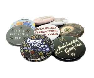 A collection of 32mm button badges featuring assorted designs, texts, and logos is displayed overlapping on a white background.