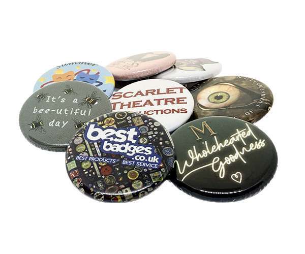 A collection of 32mm button badges featuring assorted designs, texts, and logos is displayed overlapping on a white background.