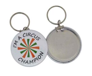 Two metal keychains; one displays the text "I'M A CIRCUS CHAMPION" with a colorful pattern, and the other shows the plain back side.