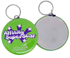 Two round keychains: one side is green with "Affinity Superstar" and stars in purple and white; the other side is blank and reflective.
