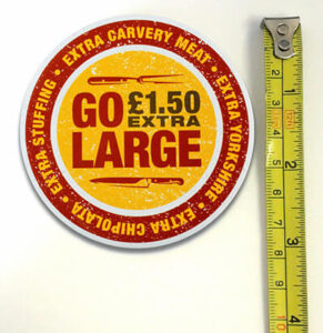 A round sign reading "GO LARGE £1.50 EXTRA" with details of extra carvery meat, Yorkshire, stuffing, and chipolata, next to a measuring tape.