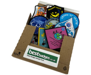 Fabric badge sample pack in a cardboard box with 3x embroidered, 3x woven, and 3x printed badges in various designs and colors. The box has a Best Badges logo sticker on a green background and the title of the pack.