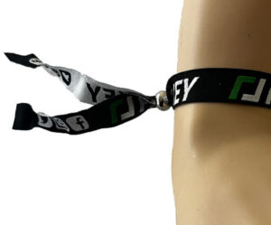 A black and white fabric wristband with green and white text and social media icons is worn on a person's wrist.