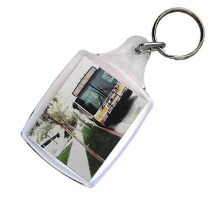 A keychain with a photo insert showing a city bus parked next to a sidewalk lined with trees.