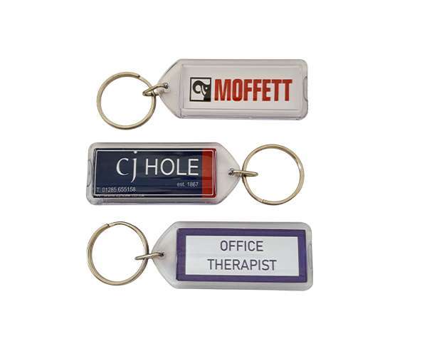 Three Acrylic Keyrings (50mm x 20mm Lozenge), each with a rectangular label—“MOFFETT,” “CJ HOLE,” and “OFFICE THERAPIST”—and attached to a metal keyring.