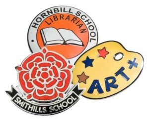 Three school badges: one for Hornbill School librarian with a book, a Smithills School badge with a red rose, and a yellow art badge with colored stars and "ART".