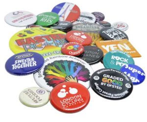 A scattered collection of colorful promotional and campaign buttons with various slogans, logos, and designs displayed on a white surface.