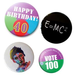 Four assorted round badges: one says "HAPPY BIRTHDAY! 40," one has "E=MC²," one features a colorful portrait, and one says "VOTE 100 Girlguiding South West England.