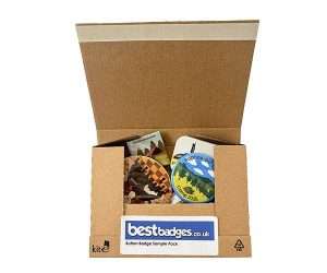 An open cardboard box containing assorted button badges, featuring a label on the front that reads “Button Badge Sample Pack”.