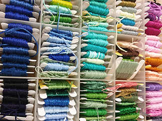 A close-up of organized embroidery floss in various colors, neatly wound on plastic bobbins and stored in a compartmentalized container.