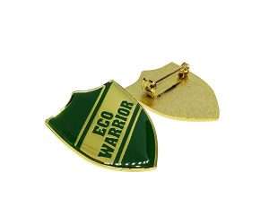 An Eco Warrior Badge, featuring a gold shield shape with green accents and the words “ECO WARRIOR” on the front, is shown alongside its reverse side with a clasp.