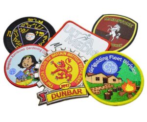 A collection of five colorful embroidered patches, including badges for clubs, teams, and events, arranged in an overlapping display.