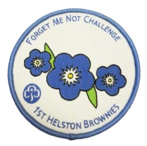 Circular woven badge featuring three blue forget-me-nots, with the text 'Forget Me Not Challenge' in blue at the top and '1st Helston Brownies' in blue at the bottom.