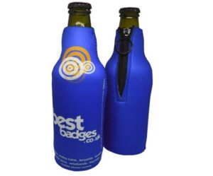 Two brown glass bottles are covered with blue neoprene sleeves; one sleeve is zipped closed, both display the "best badges" logo and website.