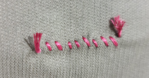 Pink embroidery thread is sewn in a zigzag pattern through grey fabric, with frayed ends visible on both sides.