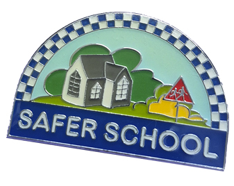 A badge with an illustration of a school building, trees, and a child crossing sign, labeled "SAFER SCHOOL" on a blue banner.