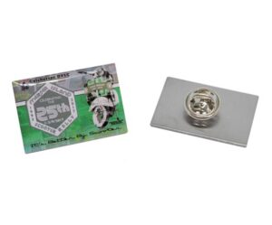 Printed metal badge showing a scooter on a green background with the text 'Mersea Islands Scooter Rally' and 'Celebrating the 25th, 1993–2017'; next to it, the back of the badge is visible, featuring a metal butterfly clutch pin.