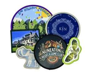 A set of seven colourful Printed Fabric Badge embroidered patches and badges, featuring a variety of designs such as landscapes, animals, club logos, and event motifs, arranged in an overlapping display on a white background.