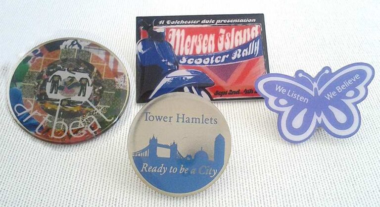 Four assorted badges are displayed on a white surface, including a circular collage, a city-themed badge, an event badge, and a purple butterfly-shaped badge with motivational text.