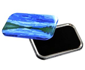 A rectangular metal tin with a blue landscape design on the lid, partially open to show a black interior.