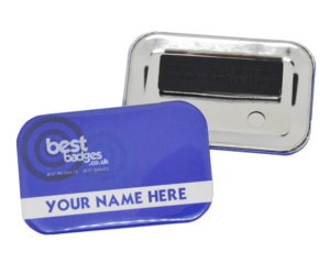 Two rectangular name badges; one shows a blue front with "YOUR NAME HERE" and "best badges.co.uk" text, the other displays the metal back with a black magnetic fastener.