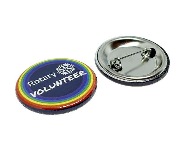 Two Rotary Volunteer Badges, one turned up to show “Rotary VOLUNTEER” with a rainbow border, and the other turned down to display the metal pin backing.