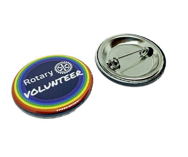 A set of two Rotary Volunteer Badges featuring round designs with rainbow borders—one displaying the “Rotary Volunteer” text and logo, and the other revealing the metal pin backing.