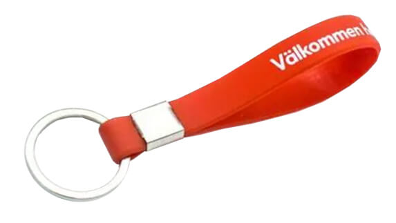 A red keychain with a metal ring and a looped strap, featuring the word "Välkommen" printed in white text.