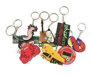 A variety of soft PVC keyrings featuring colourful designs—such as animals, cartoon characters, vehicles, and promotional logos—are displayed overlapping each other on a white background.