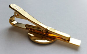 A gold tie clip with a round base is placed on a plain light-colored surface.