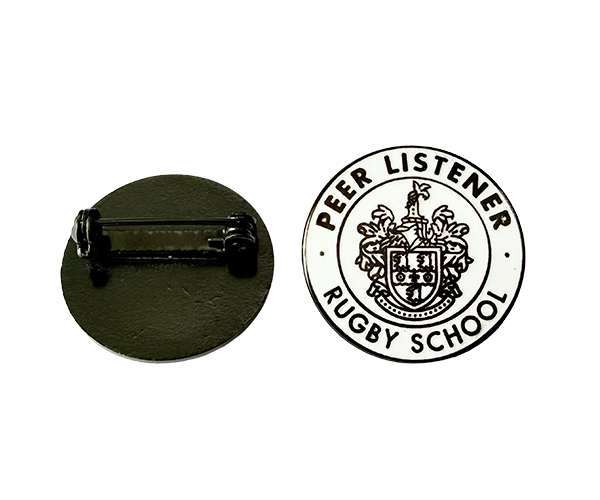 Two Traditional Hard Enamel Badges; one displays the back with a pin, whilst the other shows “Peer Listener Rugby School” and a crest on the front.