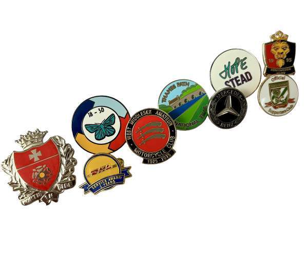 Seven Traditional Hard Enamel Badges, featuring a range of logos, emblems, and text designs, are arranged in a curved line on a white background.