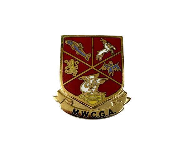 A Traditional Hard Enamel Badge in gold and red, shield-shaped, featuring four animal symbols and the letters "M.W.C.G.A." on a banner at the bottom.