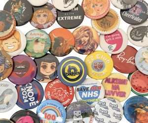 A set of Unique Design Button Badges – Every Badge Different – showcasing vibrant text, cartoon characters, logos, and illustrations arranged closely together on a white surface.
