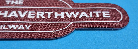Close-up of a maroon embroidered patch with partial white text reading "HAVERTHWAITE" on a blue background.
