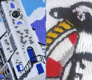 Close-up of two embroidered patches: one shows a stone clock tower with blue sky, the other depicts a black-and-white bird with a red and yellow detail.