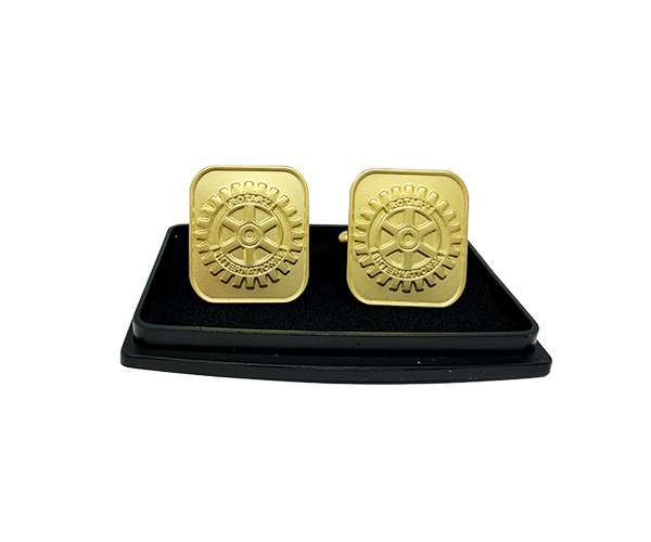A pair of Rotary Gold Cufflinks, featuring gold-tone square design engraved with a rotary gear symbol and text, is presented on a black rectangular display tray against a white background.