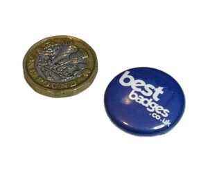 A British one-pound coin next to a blue button badge with the white text “best badges .co.uk” on it.
