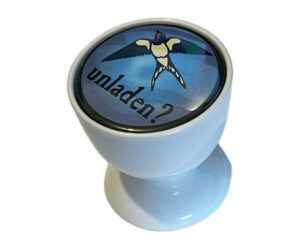 A white egg cup with a badge on top featuring a flying swallow and the word "unladen?" written in black text on a blue background.