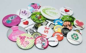 A collection of colourful round pin badges with various designs and text, arranged on a light surface.