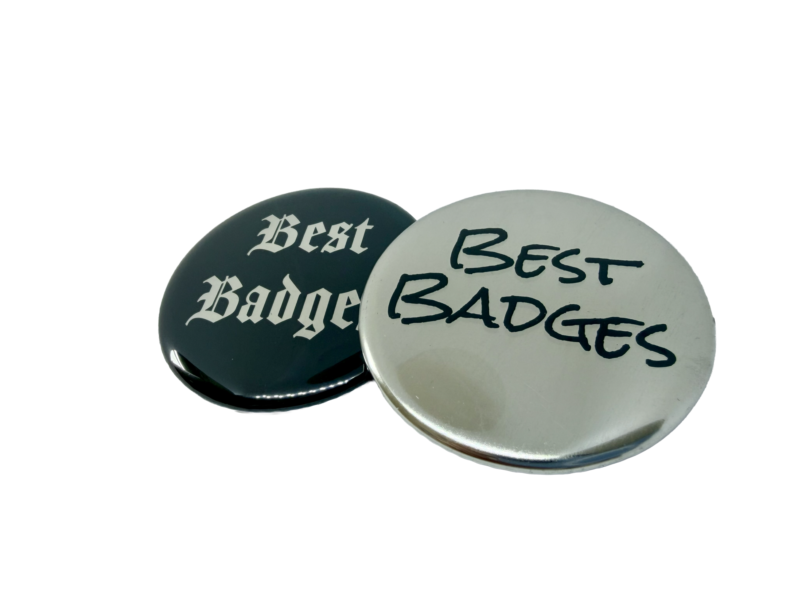Two round Metallic Button Badges displayed on a white background. One features a black finish with "Best Badge" in gothic script, whilst the other has a silver finish with "Best BADGES" in bold, black marker-style lettering. These Metallic Button Badges are the perfect inspiration for designing your own and expressing your unique style.
