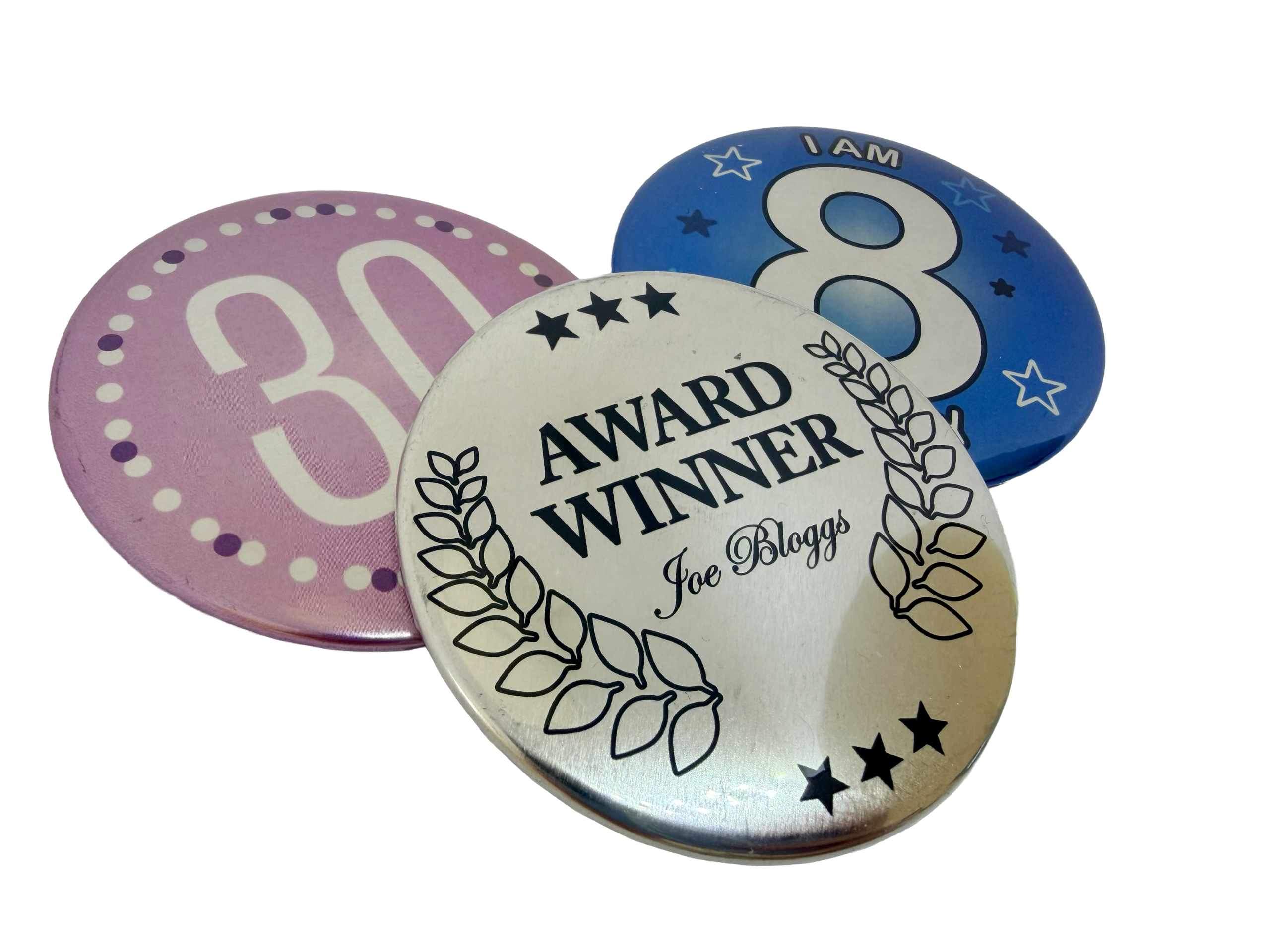Three Metallic Button Badges are displayed: a pink one with "30," a blue one featuring "I AM 8," and a silver badge reading "AWARD WINNER Joe Bloggs" surrounded by stars and laurel leaves—perfect inspiration if you’d like to design your own Metallic Button Badge.