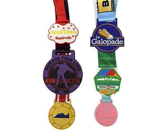 Five colourful Soft PVC Medals hang from ribbons, each featuring different designs and logos—including running shoes, animals, event names, and unique soft PVC details.