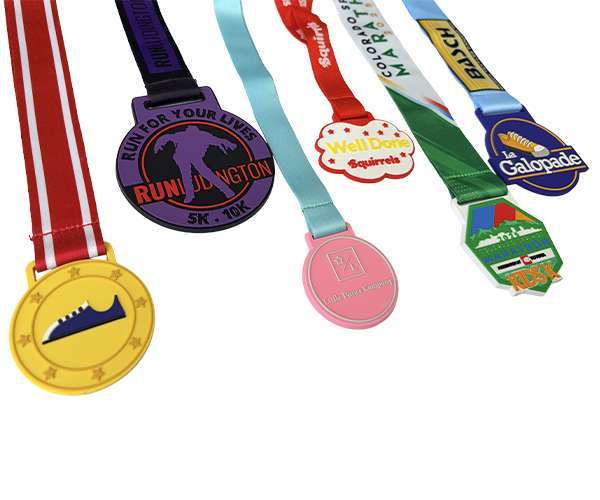 Five colourful Soft PVC Medals with ribbons, each showcasing unique designs—including a trainer, a cityscape, a squirrel, and various text—are displayed against a white background.