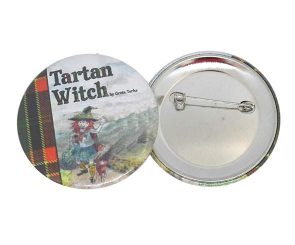 Two round pin-back buttons, one showing the text "Tartan Witch by Greta Yorke" with an illustration of a witch in tartan clothing, and the other showing the back side with a safety pin.
